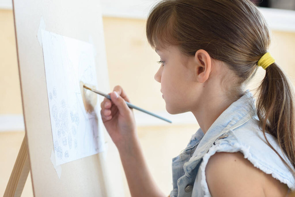 8歳の少女がイーゼルに筆の模様を描く - 写真・画像