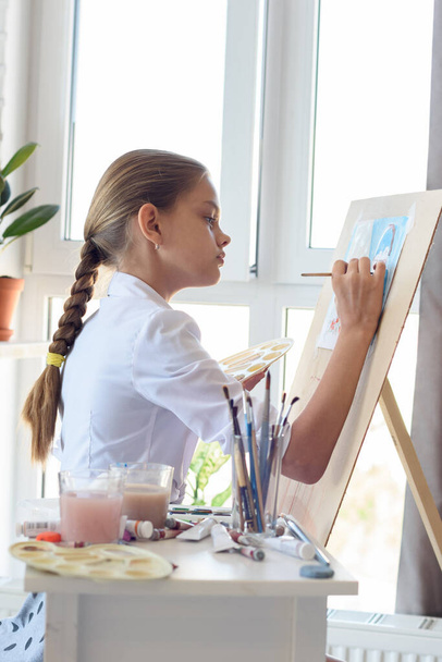 Girl in white shirt draws behind easel with right hand - Foto, imagen