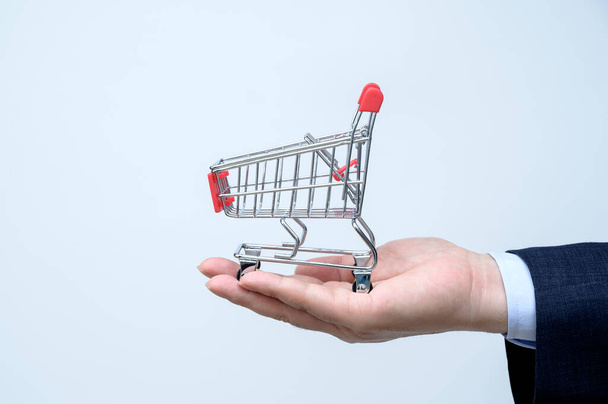 Man in suit holding small shopping trolley in hand. Close up. Business, commerce and shopping concept. - Foto, Imagem