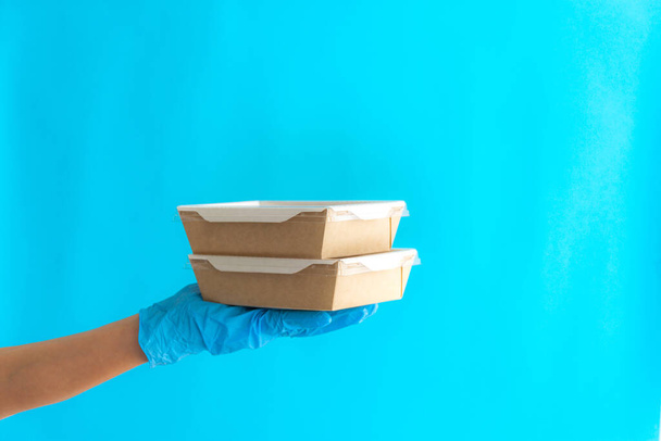 Koerier levering van voedsel in containers. Koerier meisje met containers op een blauwe achtergrond. Levering bij zelfisolatie. Een vrijwilliger levert eten. Het concept van voedsellevering. Afhaalmaaltijden. - Foto, afbeelding