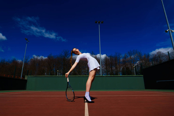 Sexy Tennisspielerin in weißem Kleid und High Heels mit Tennisschläger auf dem Platz. Junge Frau spielt Tennis, Sport - Foto, Bild