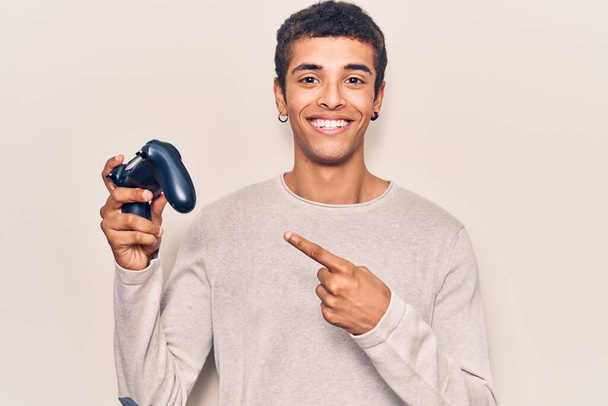 Молодий афроамериканський чоловік грає в відеогру, тримаючи контролер усміхненим щасливим вказівником рукою і пальцем
  - Фото, зображення