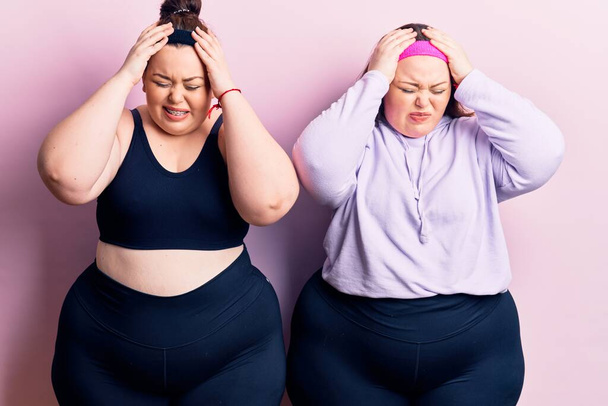 Young plus size twins wearing sportswear suffering from headache desperate and stressed because pain and migraine. hands on head.  - Foto, Imagen