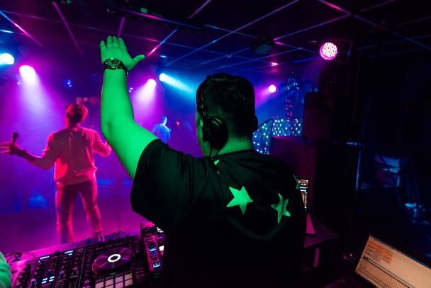 πλάτη ενός αρσενικού DJ με σηκωμένο χέρι σε ακουστικά σε ηλεκτρονική συναυλία - Φωτογραφία, εικόνα