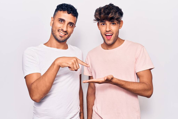 Jeune couple gay portant des vêtements décontractés étonné et souriant à la caméra tout en présentant avec la main et pointant du doigt.  - Photo, image