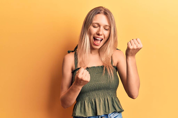 Jeune femme blonde portant des vêtements décontractés célébrant surpris et étonnés pour le succès avec les bras levés et les yeux fermés  - Photo, image