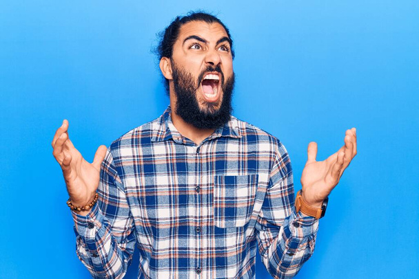 Young arab man wearing casual clothes crazy and mad shouting and yelling with aggressive expression and arms raised. frustration concept.  - Foto, Bild