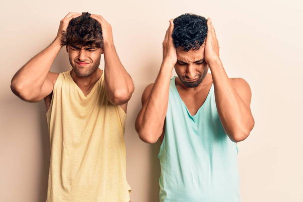 Mladý homosexuální pár v neformálním oblečení, trpící bolestí hlavy, zoufalý a vystresovaný, protože trpí bolestí a migrénou. Ruce za hlavu.  - Fotografie, Obrázek