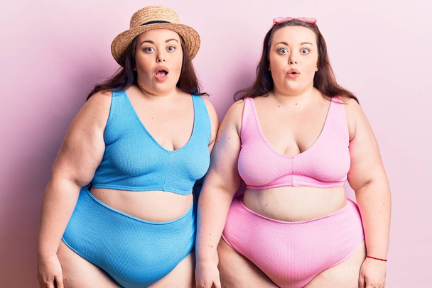 Young plus size twins wearing bikini scared and amazed with open mouth for surprise, disbelief face  - Foto, imagen