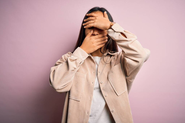 Young beautiful asian woman wearing casual shirt standing over pink background Covering eyes and mouth with hands, surprised and shocked. Hiding emotion - Photo, Image