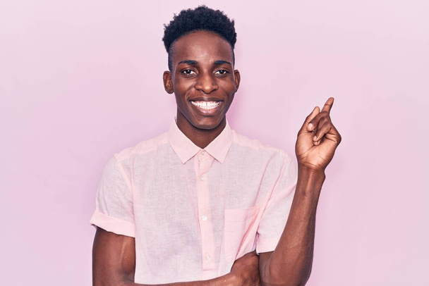 Jovem afro-americano vestindo roupas casuais sorrindo feliz apontando com a mão e o dedo para o lado  - Foto, Imagem
