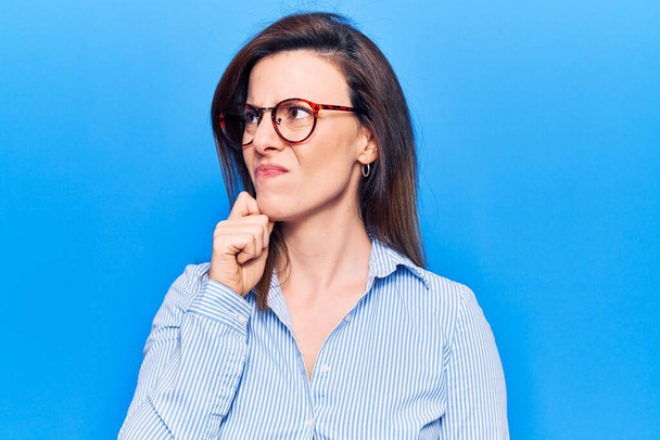 Молодая красивая женщина в деловой одежде и очках, думая о сомнении с пальцем на подбородок и глядя вверх интересно  - Фото, изображение