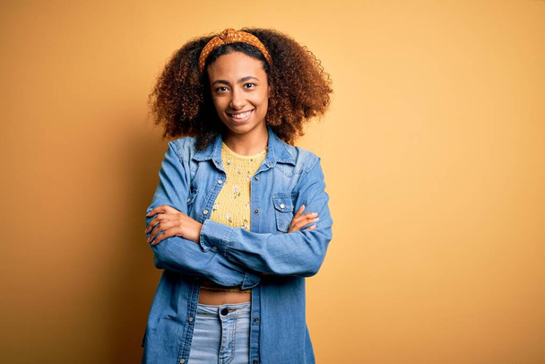 Beautiful african american with afro hair standing over yellow isolated background happy face smiling with crossed arms looking at the camera. Positive person. - Photo, image