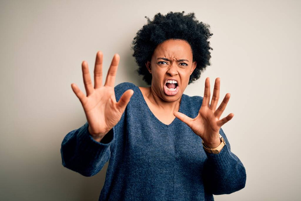 Joven hermosa afroamericana afro mujer con el pelo rizado con suéter casual miedo y aterrorizado con la expresión de miedo detener el gesto con las manos, gritando en shock. Concepto de pánico
. - Foto, imagen