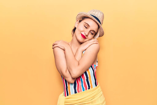 Young beautiful blonde woman wearing swimwear and summer hat hugging oneself happy and positive, smiling confident. self love and self care  - Foto, Imagem