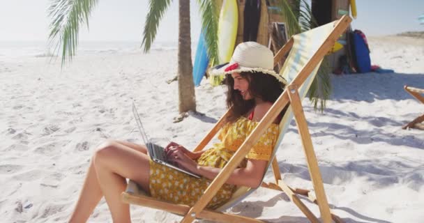 Λευκή γυναίκα απολαμβάνει το χρόνο στην παραλία, κάθεται σε μια ξαπλώστρα και χρησιμοποιεί το laptop της σε μια ηλιόλουστη μέρα σε αργή κίνηση. Χαλαρωτικές διακοπές Summer Beach. - Πλάνα, βίντεο