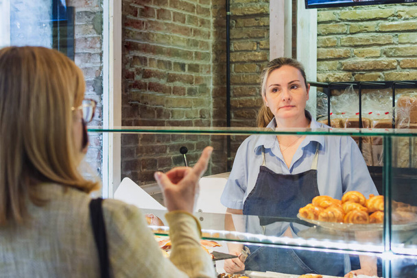 vendedora sirve cliente detrás del mostrador de panadería
 - Foto, Imagen