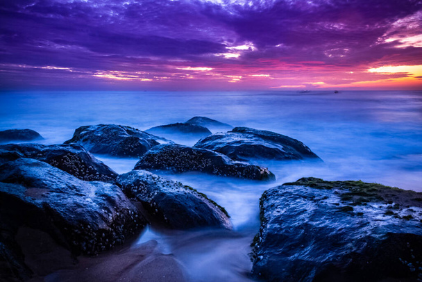 Piękny wschód słońca nad plażą w długiej ekspozycji. Przenoszenie elementów wschodzie słońca i fali fotografii z kamienistej plaży w Indiach. Czerwone niebo w zatoce bengalskiej, wolno migające fale morskie i skały. - Zdjęcie, obraz