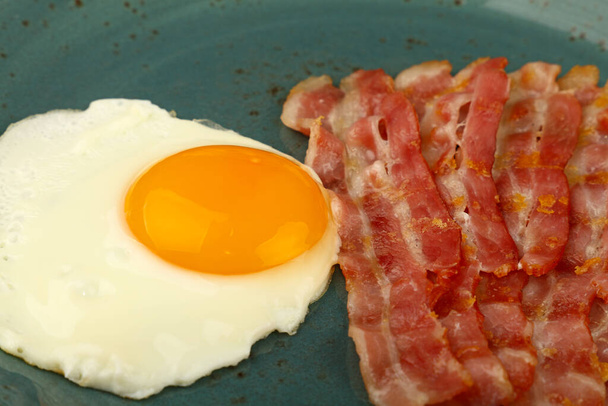 Close-up Engels ontbijt, zonnig kant ei en geroosterd spek plakjes op blauwe plaat, hoge hoek uitzicht - Foto, afbeelding