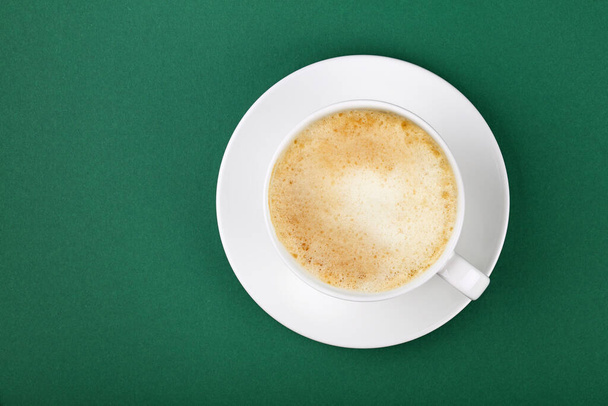 Bir fincan dolusu köpüklü latte cappuccino kapuçinoyu yeşil masa arkaplanındaki çay tabağının üzerine koy, üst manzarası yüksek, tam üstte. - Fotoğraf, Görsel