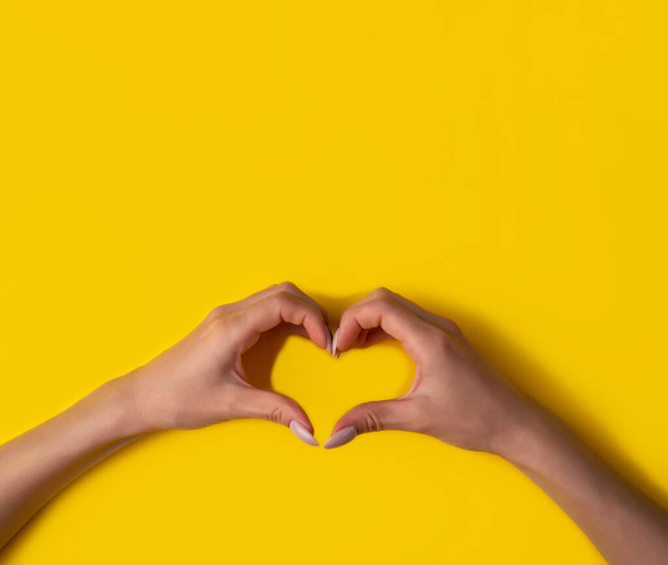 heart making woman's hands with manicure on yellow background, top view.The concept of love for your work and a beautiful manicure. Flat lay,banner - Foto, immagini