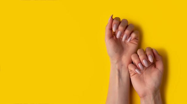 Female hands with a beautiful manicure on a yellow background,top view,flat lay. Manicure concept, banner - Foto, afbeelding