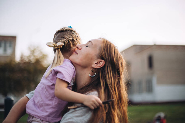 Happy woman holding her little daughter, outdoors on sunset, beautiful woman hugs her little daughter, smiling face, portrait - Photo, Image