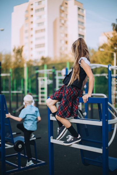 Two friends, girl and boy, are playing after school on sports playground, wearing school uniform, having fun, playing hide and seek, 8 years old - Fotoğraf, Görsel