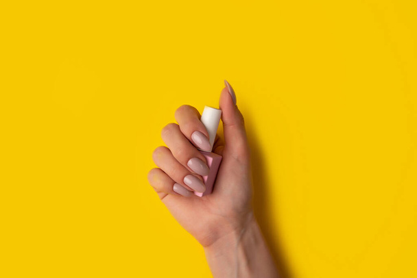 Gel polish of pink color in a hand on a yellow background, top view. Woman holds in hands pink bottle of varnish on a yellow background. Manicure concept - Photo, image