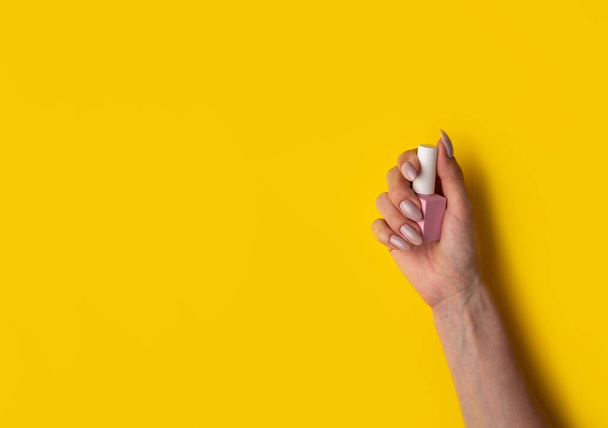 Gel polish of pink color in a hand on a yellow background, top view. Woman holds in hands pink bottle of varnish on a yellow background. Manicure concept,banner - Fotoğraf, Görsel