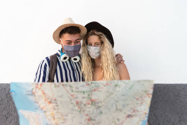 若いカップルがフェイスマスクを着用し、旅行マップを保持-コロナウイルス発生後の最初の旅行を楽しんでいる旅行者-観光と愛の関係の休暇のライフスタイルの概念を再起動 - 写真・画像