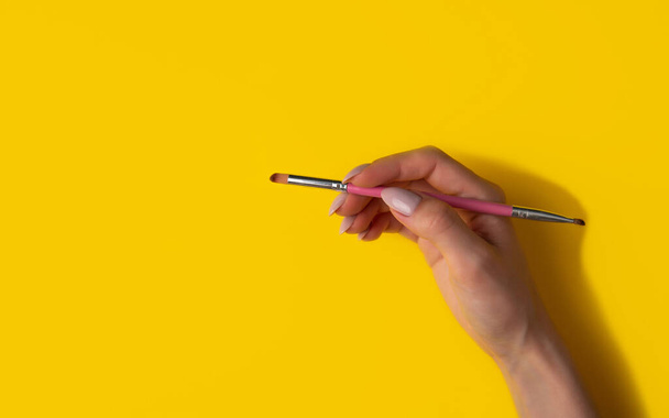 Female hand with a brush on a yellow background, top view.Manicure concept, flat lay,banner - Fotoğraf, Görsel