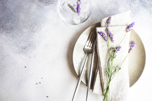 Summer time table set with minimalistic stoneware and cutlery served on concrete background and decorated with fresh lavender flowers - Foto, Imagem