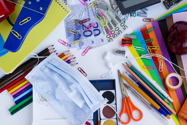 Colorful school supplies on the white surface with face mask. - Photo, Image