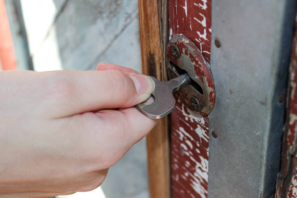 Το χέρι ανοίγει την κλειδαριά κλειδί στην παλιά πόρτα. - Φωτογραφία, εικόνα