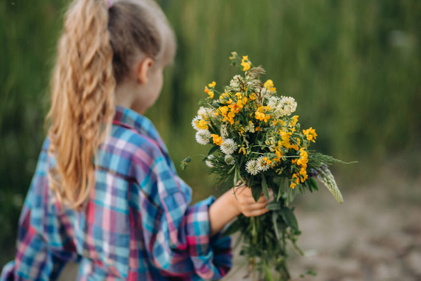 Little girl walking with bouquet of wildflowers, summer evening in countryside - Foto, Imagem