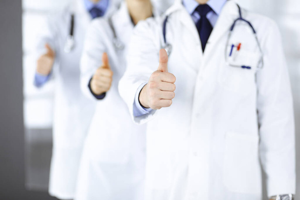 Group of unknown doctors stand as a team with thumbs up in a hospital office. Physicians ready to examine and help patients. Medical help, insurance in health care, best desease treatment and medicine - Foto, afbeelding