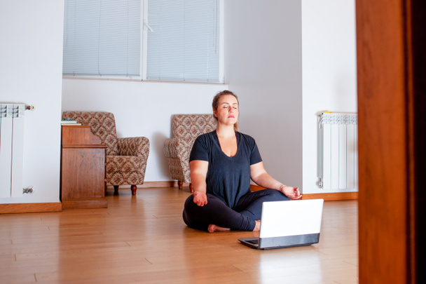 Плюс розмір жінка практикує йогу у своїй вітальні. Вона дивиться відео уроки на своєму комп'ютері. Копіювати простір
 - Фото, зображення