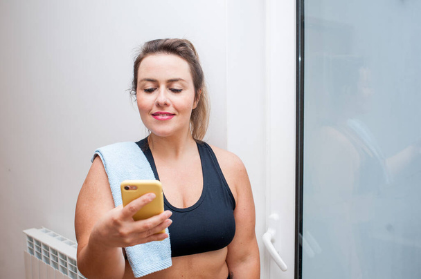 Mujer de talla grande mirando su teléfono celular después de hacer ejercicio. Tiene una toalla azul en el hombro. Copiar espacio
 - Foto, imagen