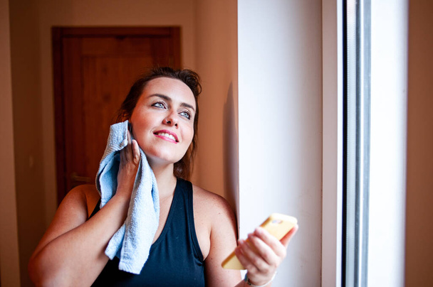 Plus size donna asciugatura sudore con un asciugamano e tenendo il suo telefono cellulare dopo l'esercizio a casa
. - Foto, immagini
