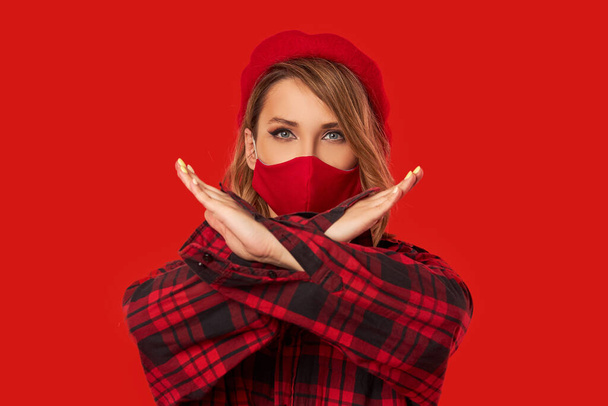 Stop covid-19. Woman in trendy fashion protective face mask during quarantine. Model in  red beret shows stop sign with hands . Monochrome look - Фото, изображение