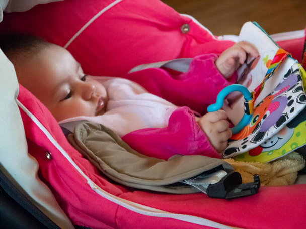 Cute little caucasian baby. She is resting on her stroller, playing with her toys. - Foto, imagen