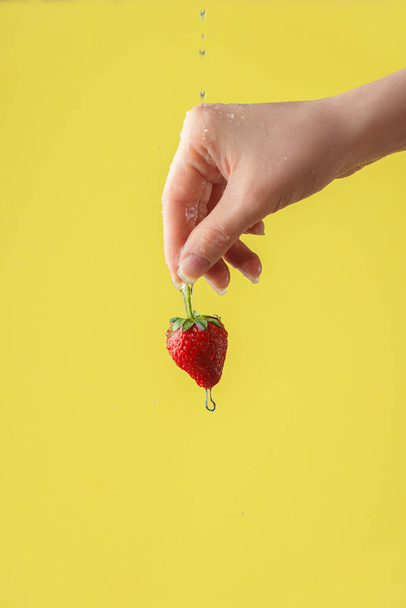 Female hands washing strawberry on the yellow saturated background. Concept of the importance of washing fruits under quarantine - Photo, image