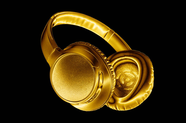 Gouden glanzende draadloze hoofdtelefoon op zwarte achtergrond geïsoleerd close-up, luxe gouden metalen bluetooth headset, moderne high-end wi-fi gele oortelefoons, audio muziek symbool, stereo geluid elektronica teken - Foto, afbeelding
