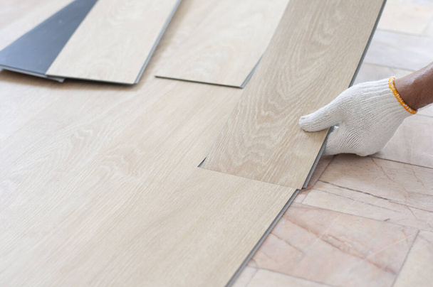 Arbeiter verlegen Holzdielen für neuen Raum. Haussanierung mit Vinylholzboden Verlegung für die Wohndekoration mit Laminat-Vinylholzboden.  - Foto, Bild