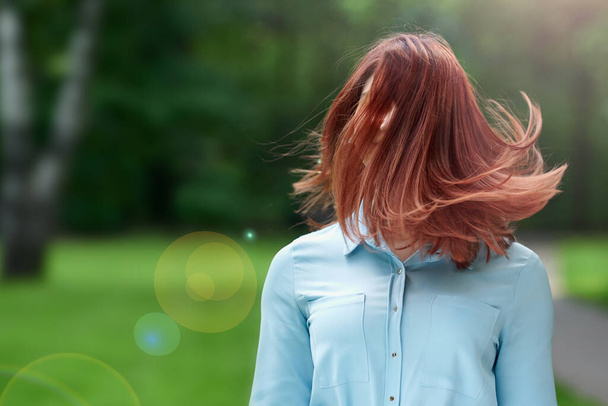 girl in a blue dress and red hair close-up on a natural green background. Flying red hair on a young girl's head in the summer - Zdjęcie, obraz