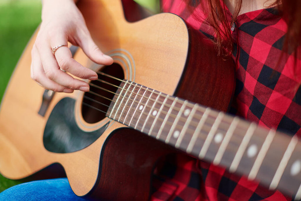 close-up of a brown classical acoustic guitar with the hand of a female musician playing the strings. Stringed musical instrument in the hands of a person close up on a blurred natural background - Photo, Image