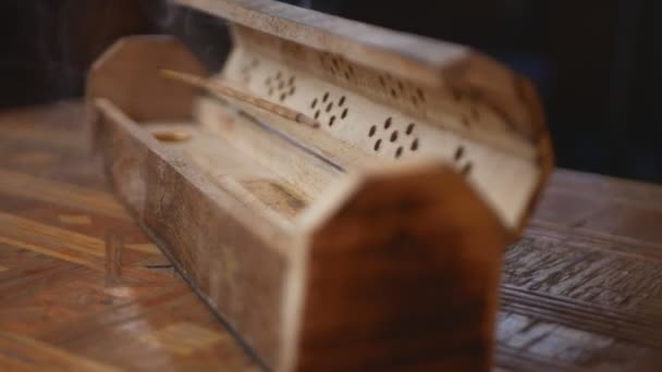 Cercueil en bois avec bâton d'encens (la fumée sort du bâton) Cône de brûleur et bâtons Boîte de support sur une table en bois faite à la main, tourne dans le sens des aiguilles d'une montre. Fond noir. Fumée. Cycle. - Séquence, vidéo