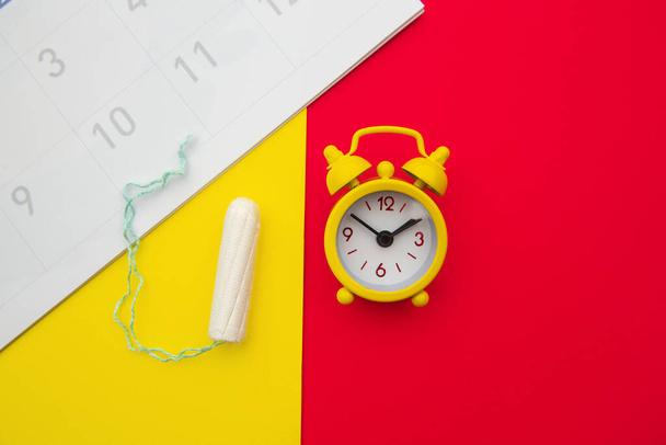 Menstrual calendar, cotton tampon and yellow alarm clock on colorful background. Females menstrual cycle concept - Photo, Image