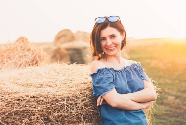 Beatiful woman smiling near haystack on field - Foto, Bild